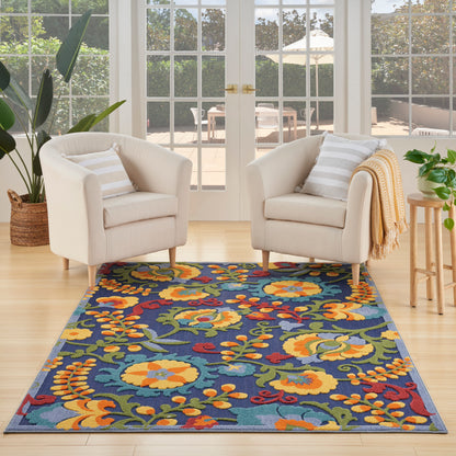 Outdoor patio scene with a blue floral outdoor rug, two beige chairs, striped cushions, a yellow throw, and glass doors.