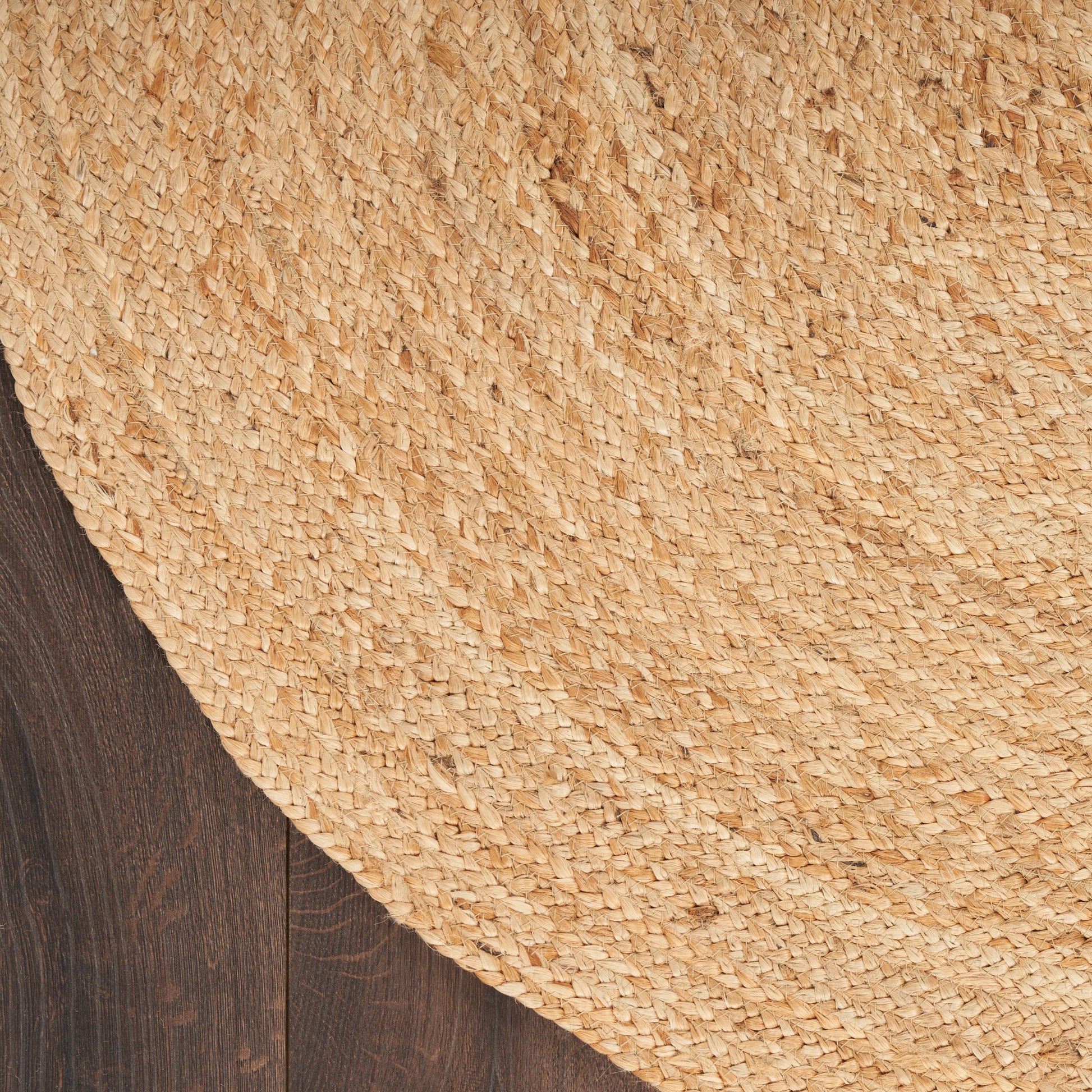 Natural woven straw circular rug on dark wood floor, textured coastal style.