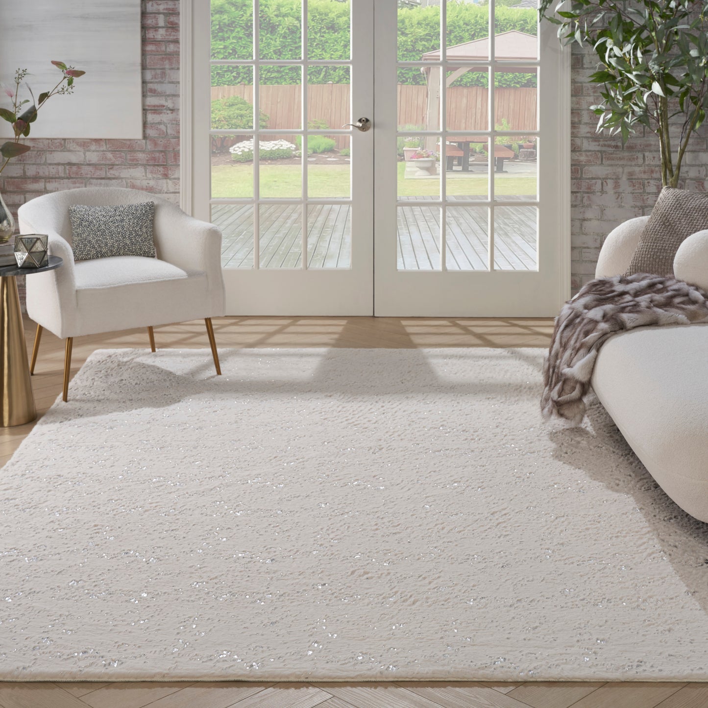 Ivory shag rug in a bright contemporary living room with cream armchairs, faux fur throw, glass French doors to garden.