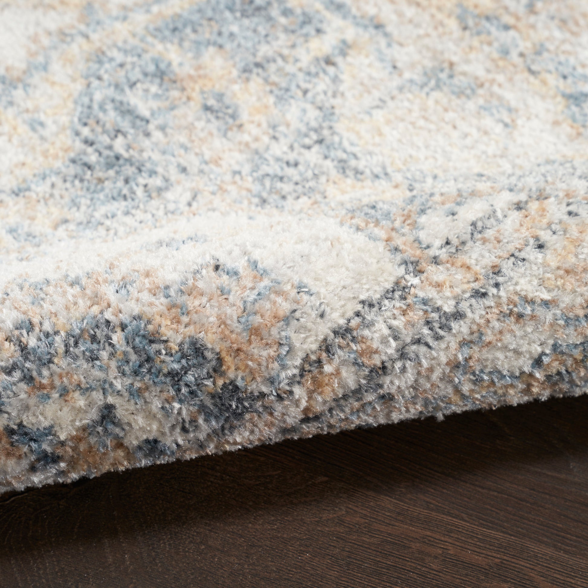 Soft shag area rug with blue, cream and tan abstract pattern; plush pile over dark wood floor.