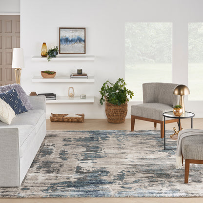 Bright living room with light gray sofa, gray accent chair, blue-gray rug, white floating shelves, brass lamp, and greenery.