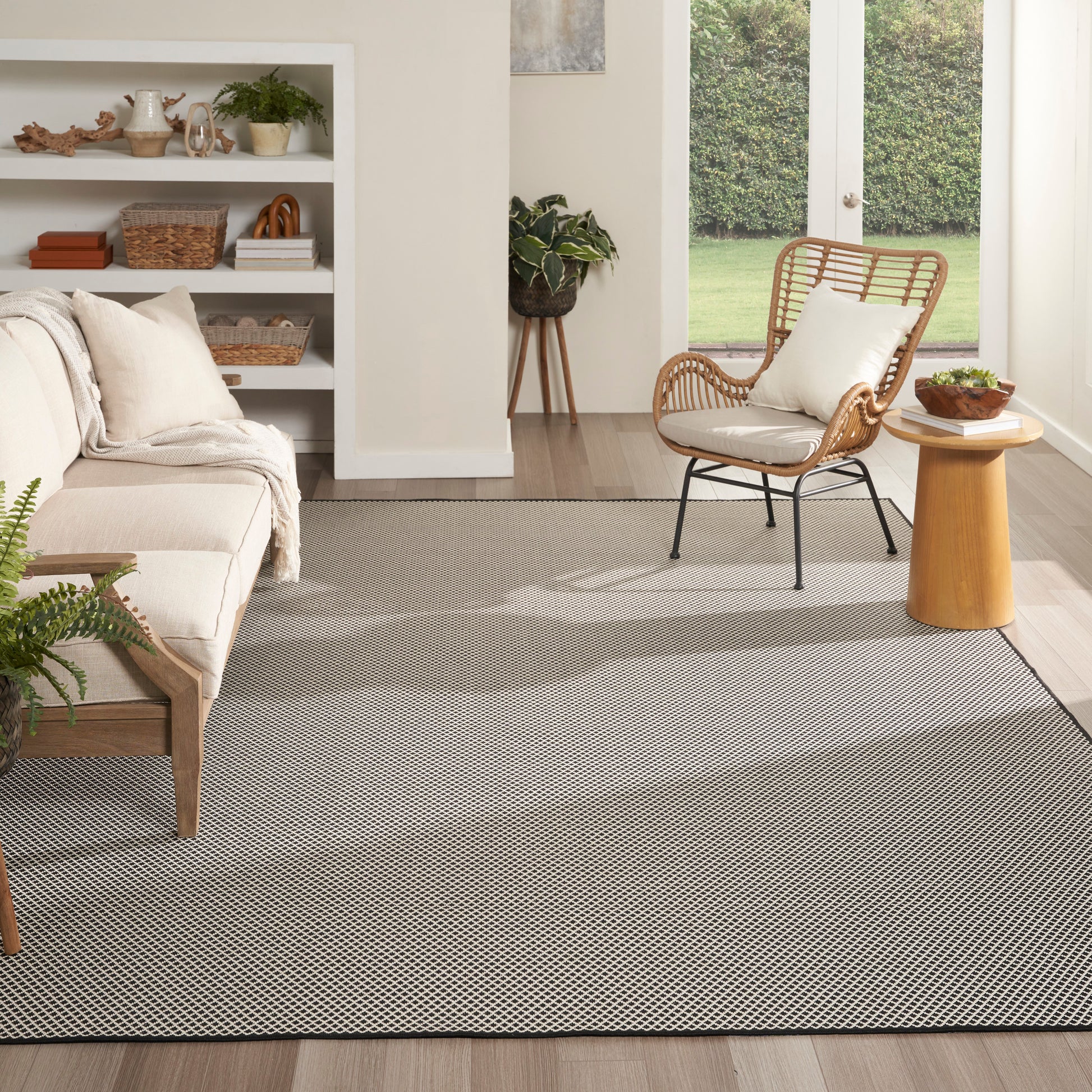 Bright living room with beige sofa, round wooden side table, gray rug, rattan chair, open shelves & plants.