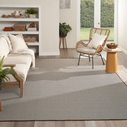 Bright living room with beige sofa, round wooden side table, gray rug, rattan chair, open shelves & plants.
