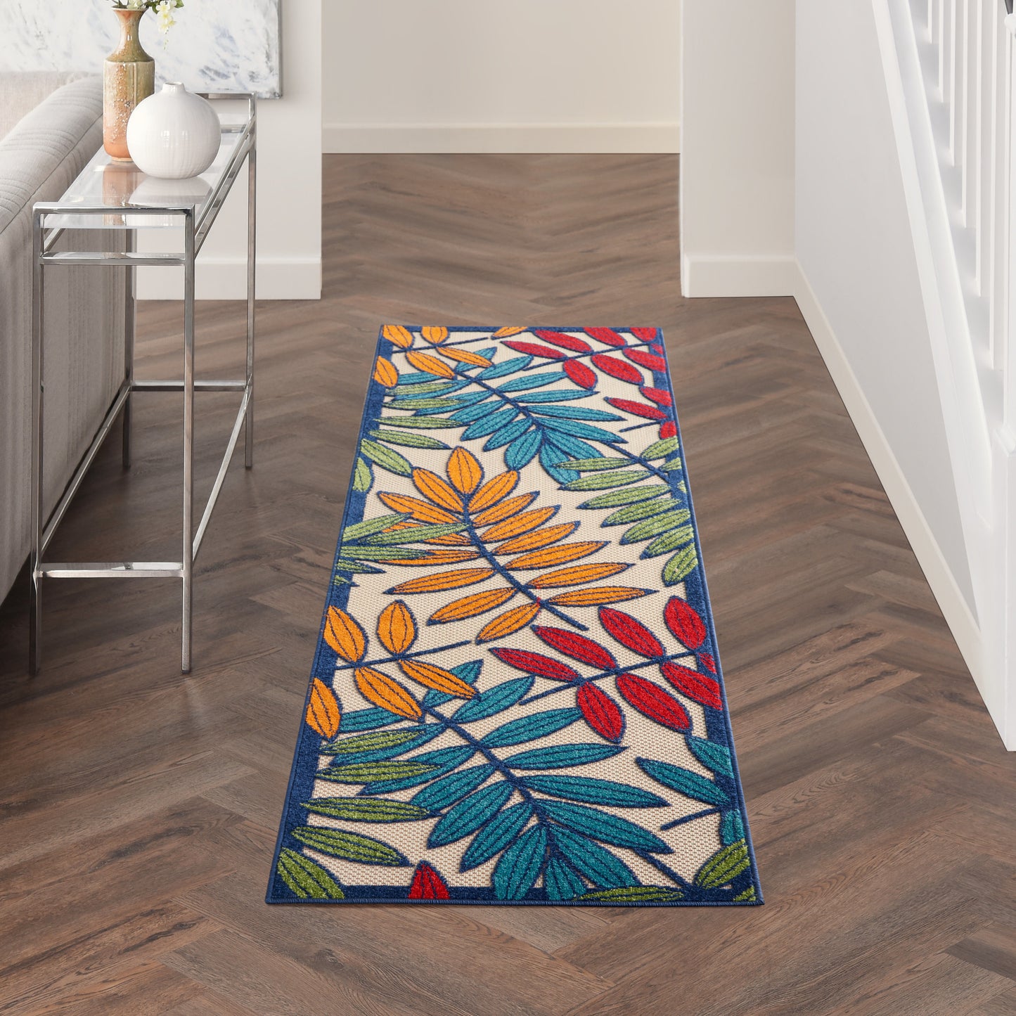 Rectangular tropical leaf runner rug with multicolor leaves on white background and a deep blue border in a modern hallway.