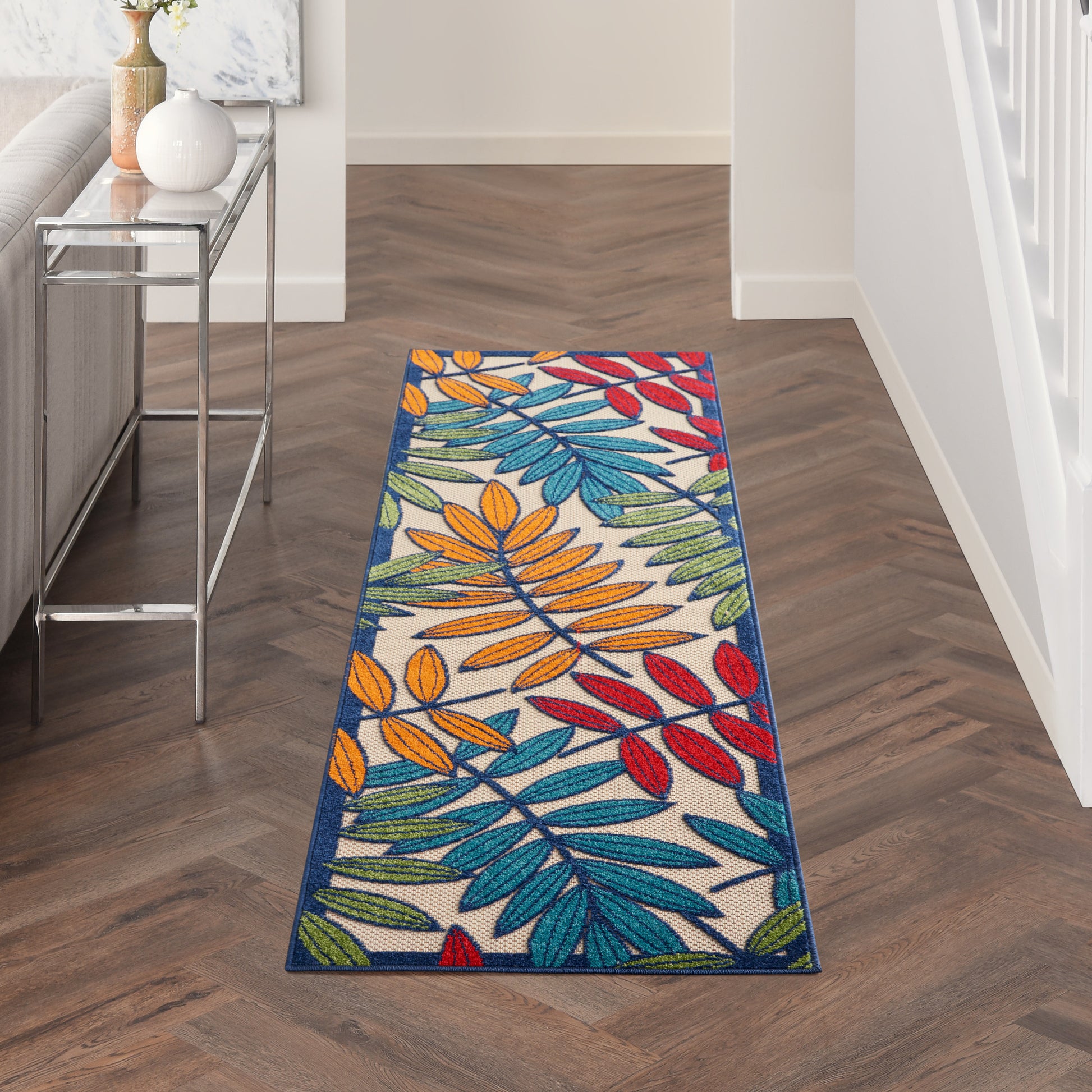 Rectangular tropical leaf runner rug with multicolor leaves on white background and a deep blue border in a modern hallway.