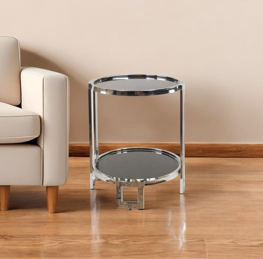 Polished chrome two-tier round mirrored glass end table with shelf beside a beige sofa.