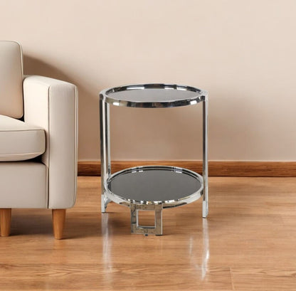 Polished chrome two-tier round mirrored glass end table with shelf beside a beige sofa.