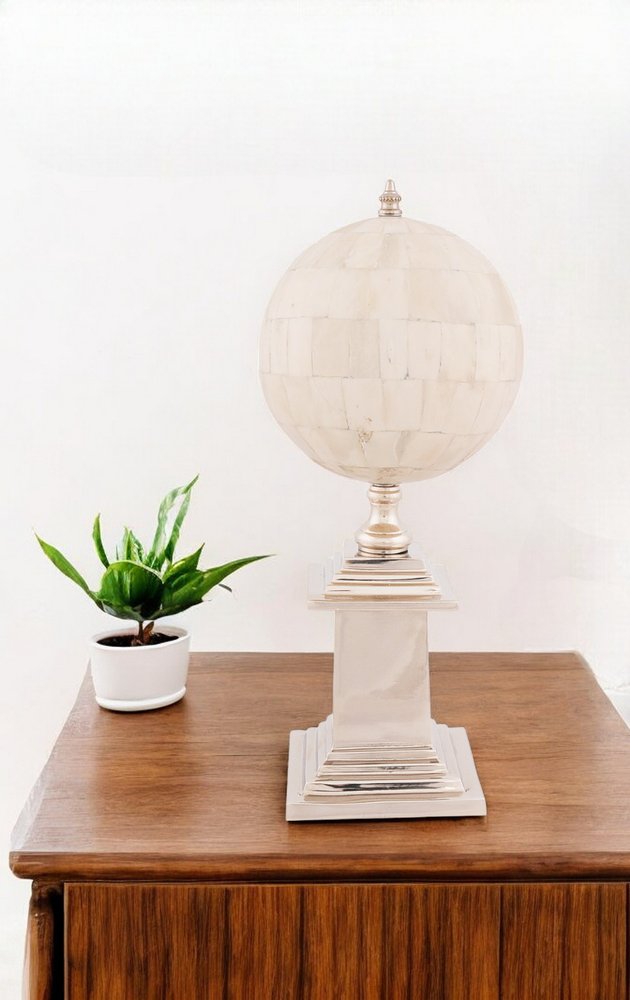 Cream globe lamp on square pedestal base atop a wooden table, beside a small white potted plant.