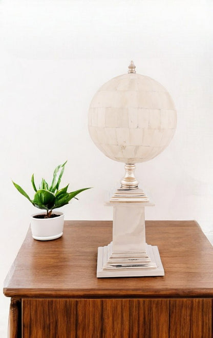 Cream globe lamp on square pedestal base atop a wooden table, beside a small white potted plant.