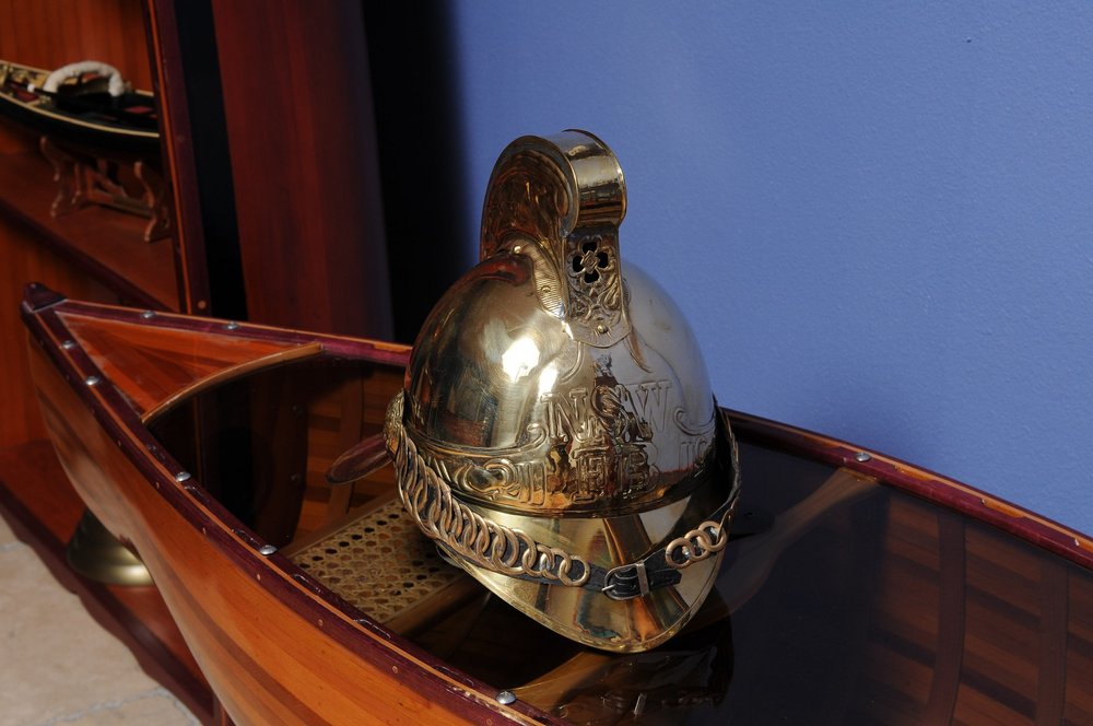 Polished brass ceremonial helmet with crest and chain trim, displayed on a wooden surface against a blue wall.
