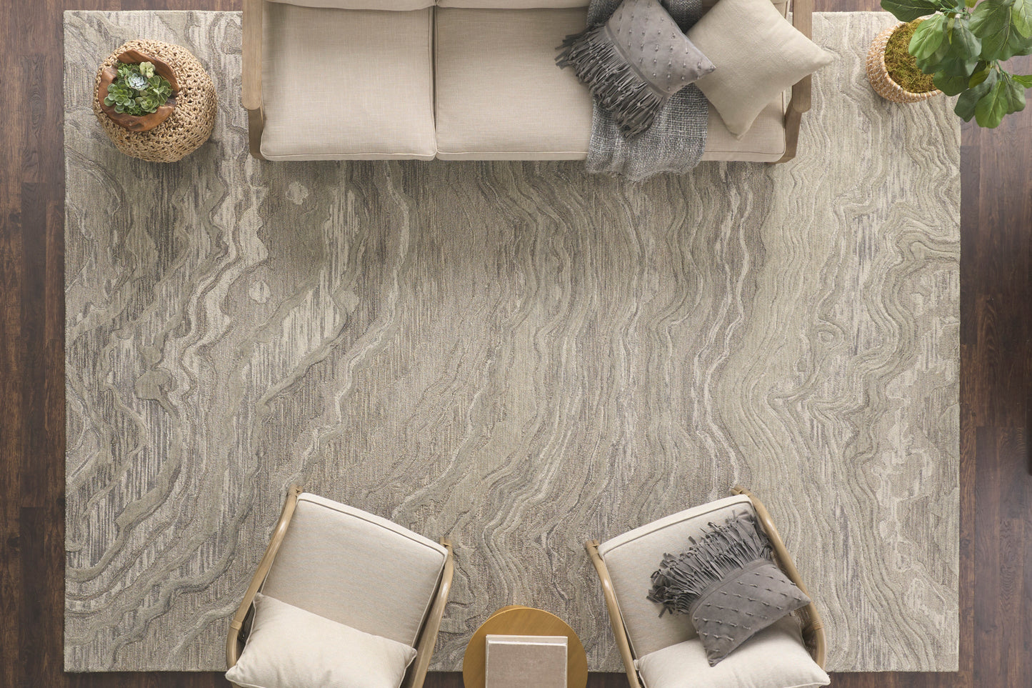 Top-down view of a light gray marbled rug with beige sofa, two armchairs, round wood coffee table, and potted plants.