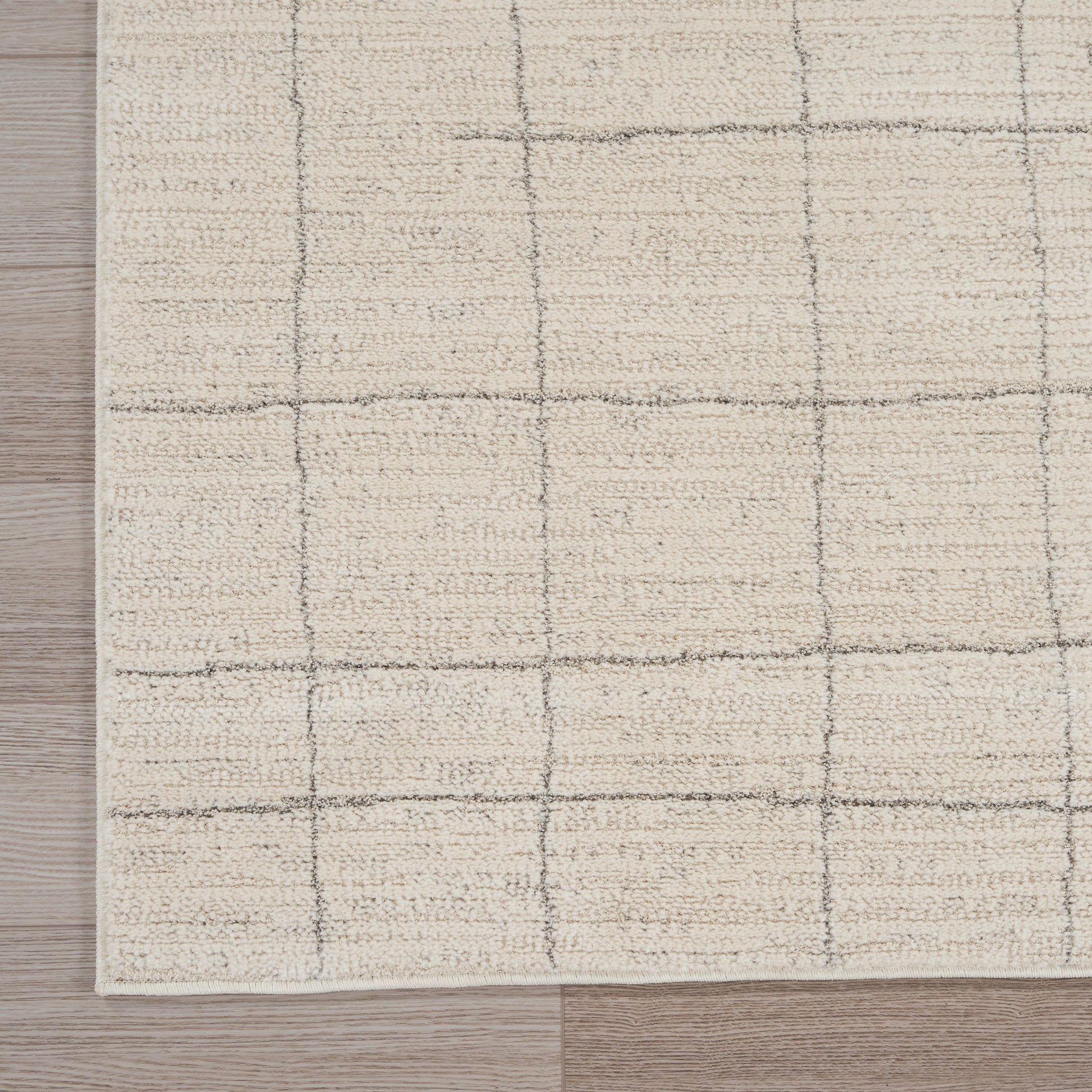 Beige textured rug with gray grid lines on light wood floor; modern geometric square pattern.