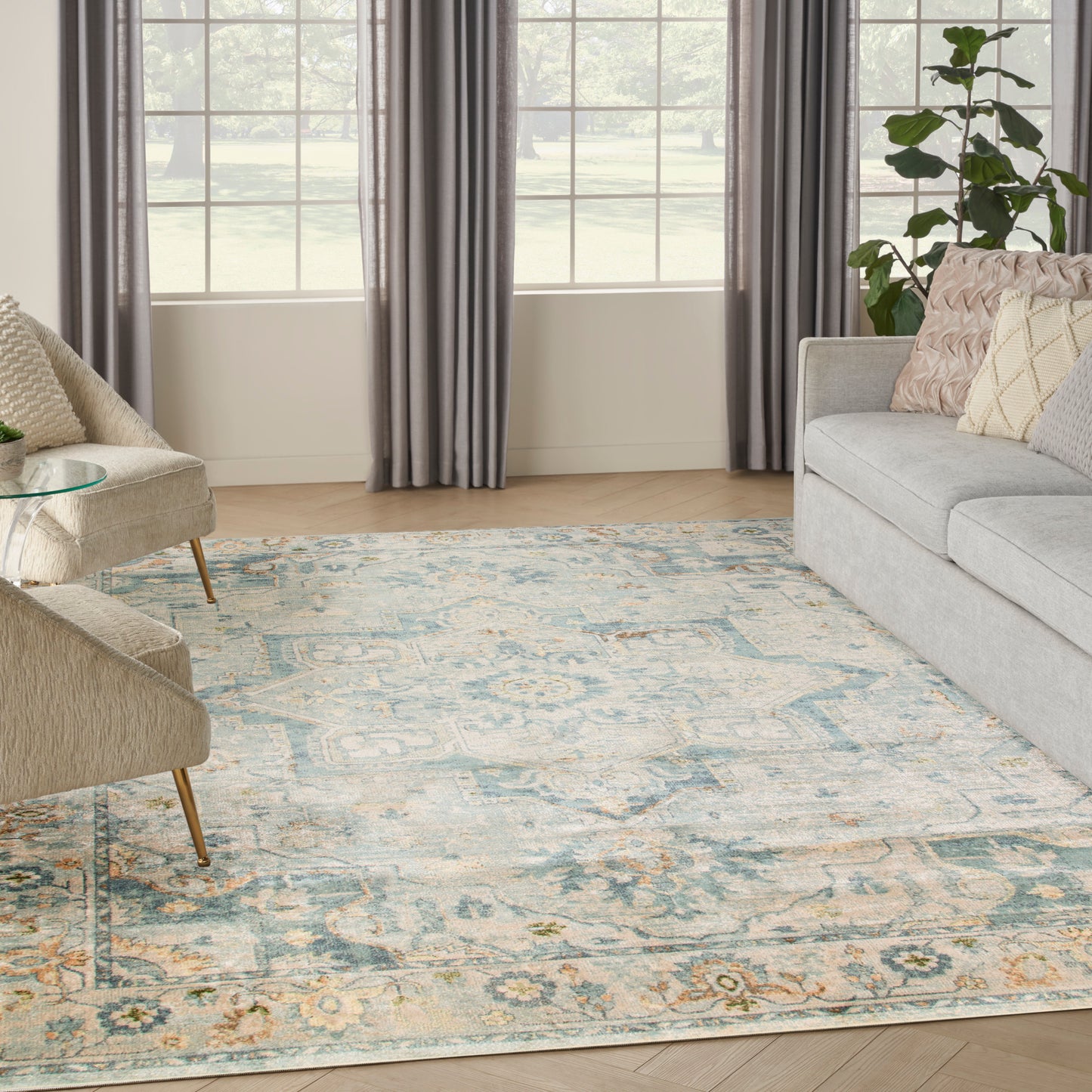 Living room with large windows, gray curtains, light gray sofa, beige chairs, glass side table, and blue-cream patterned rug.