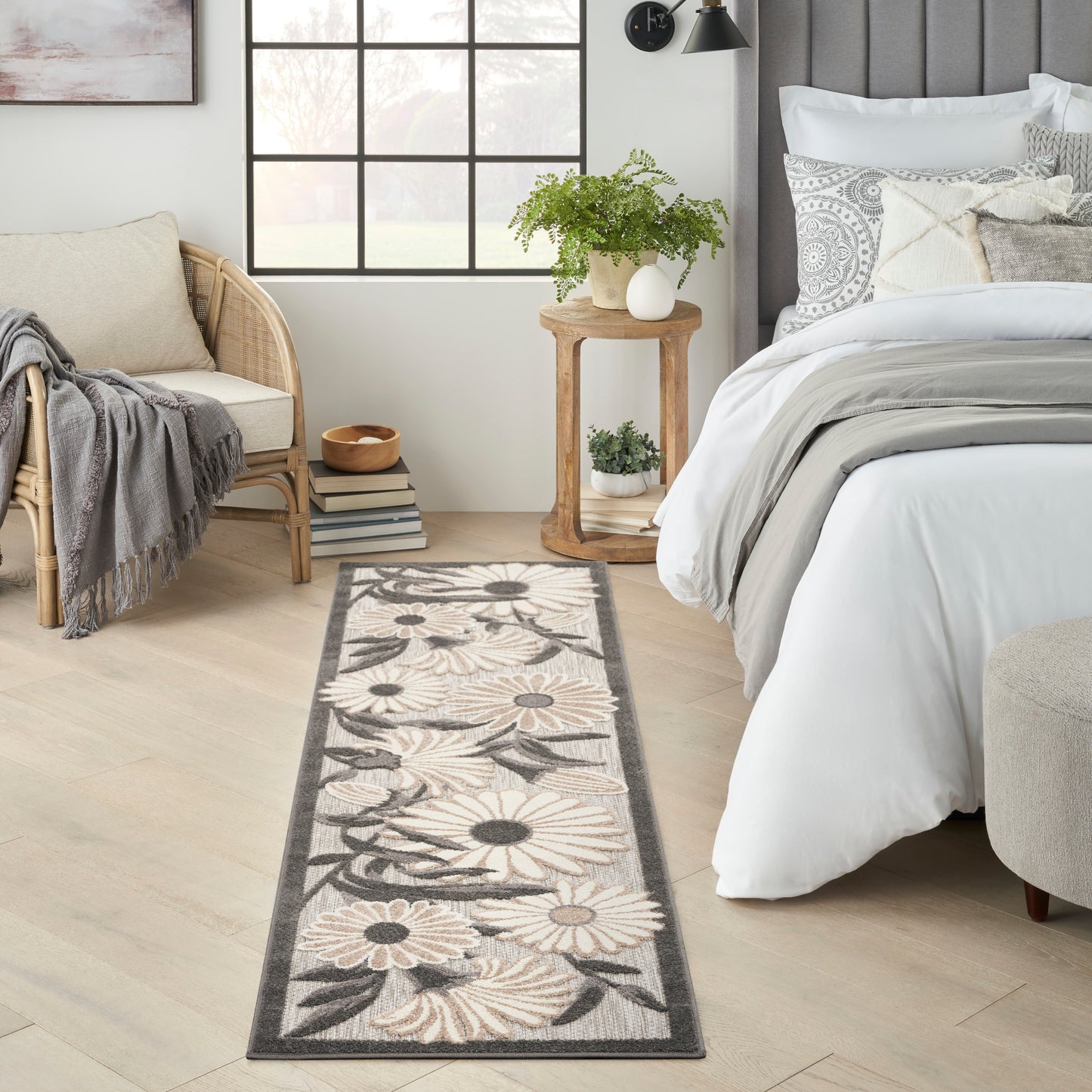 Long woven floral runner rug in beige, cream and gray with daisy pattern beside a bed in a light, airy bedroom.