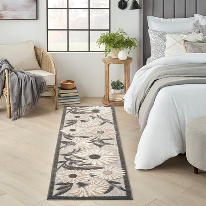Long woven floral runner rug in beige, cream and gray with daisy pattern beside a bed in a light, airy bedroom.