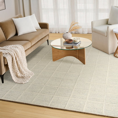 Living room with tan sofa, white pillows, cream armchair, glass-top round coffee table and beige grid rug