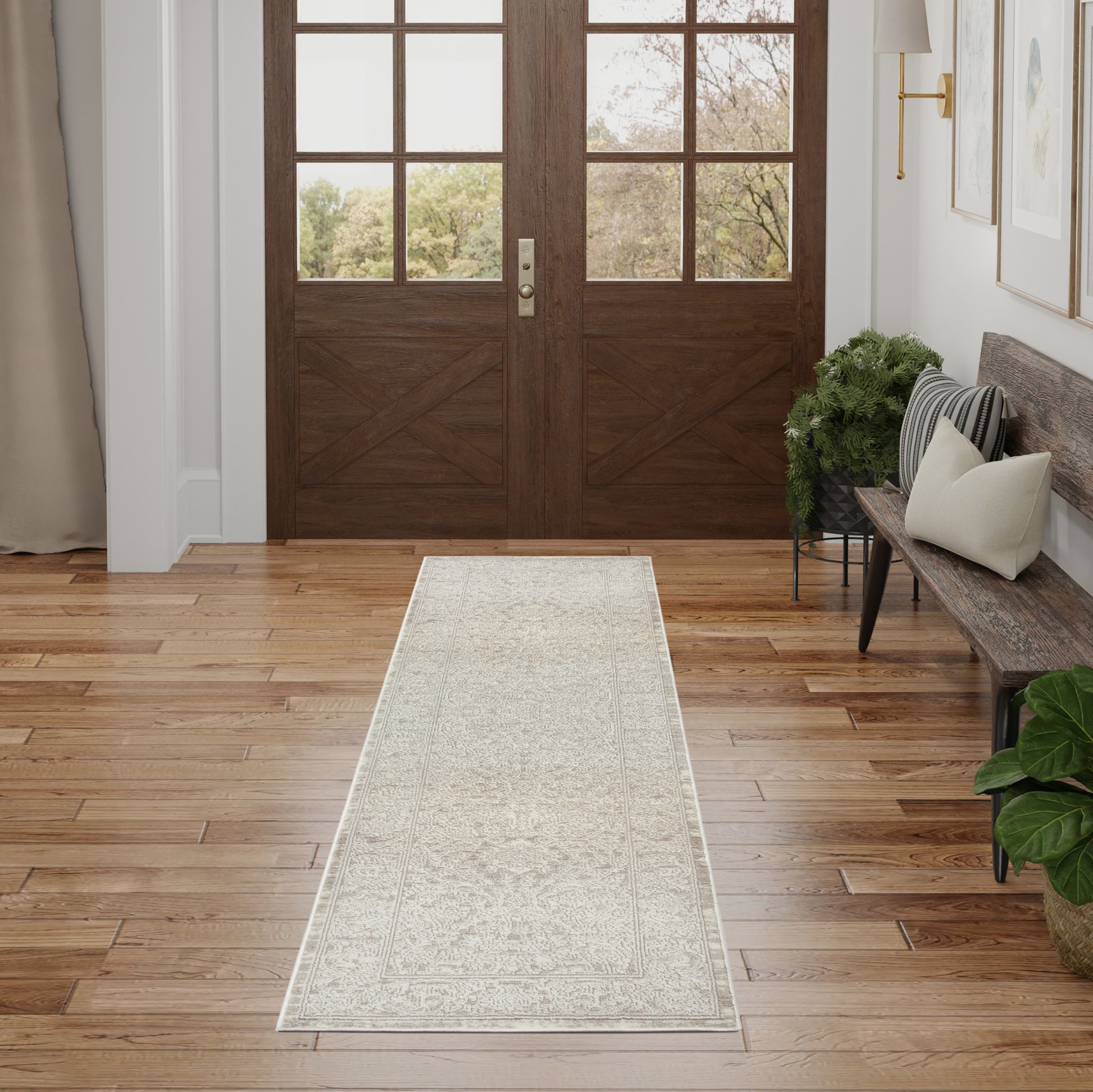 Long light-gray patterned runner rug in a foyer with wooden floors, a bench, plants, and double wood doors.