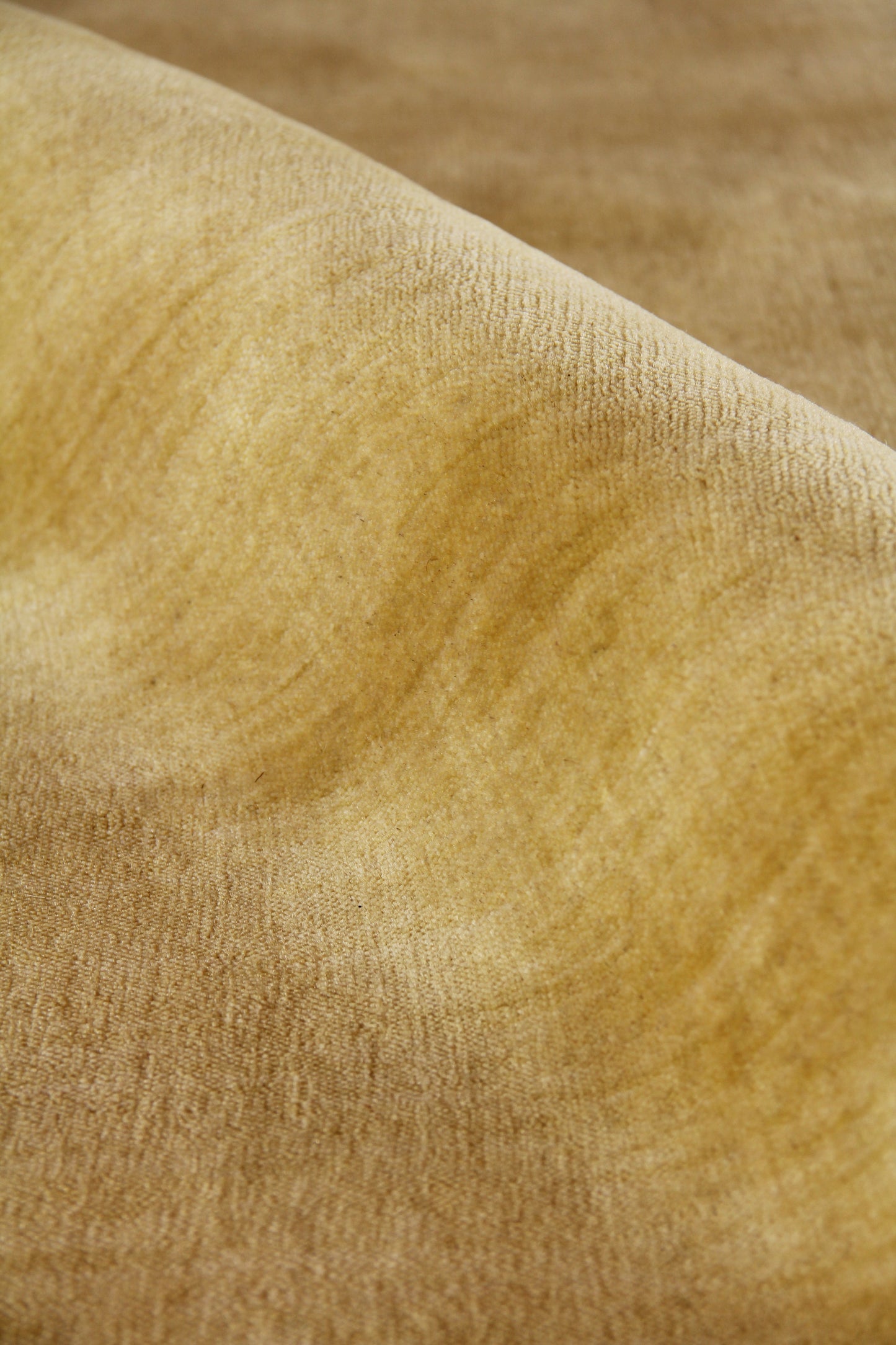 Close-up of warm golden-tan wool rug fibers with a soft nap and curving folds.