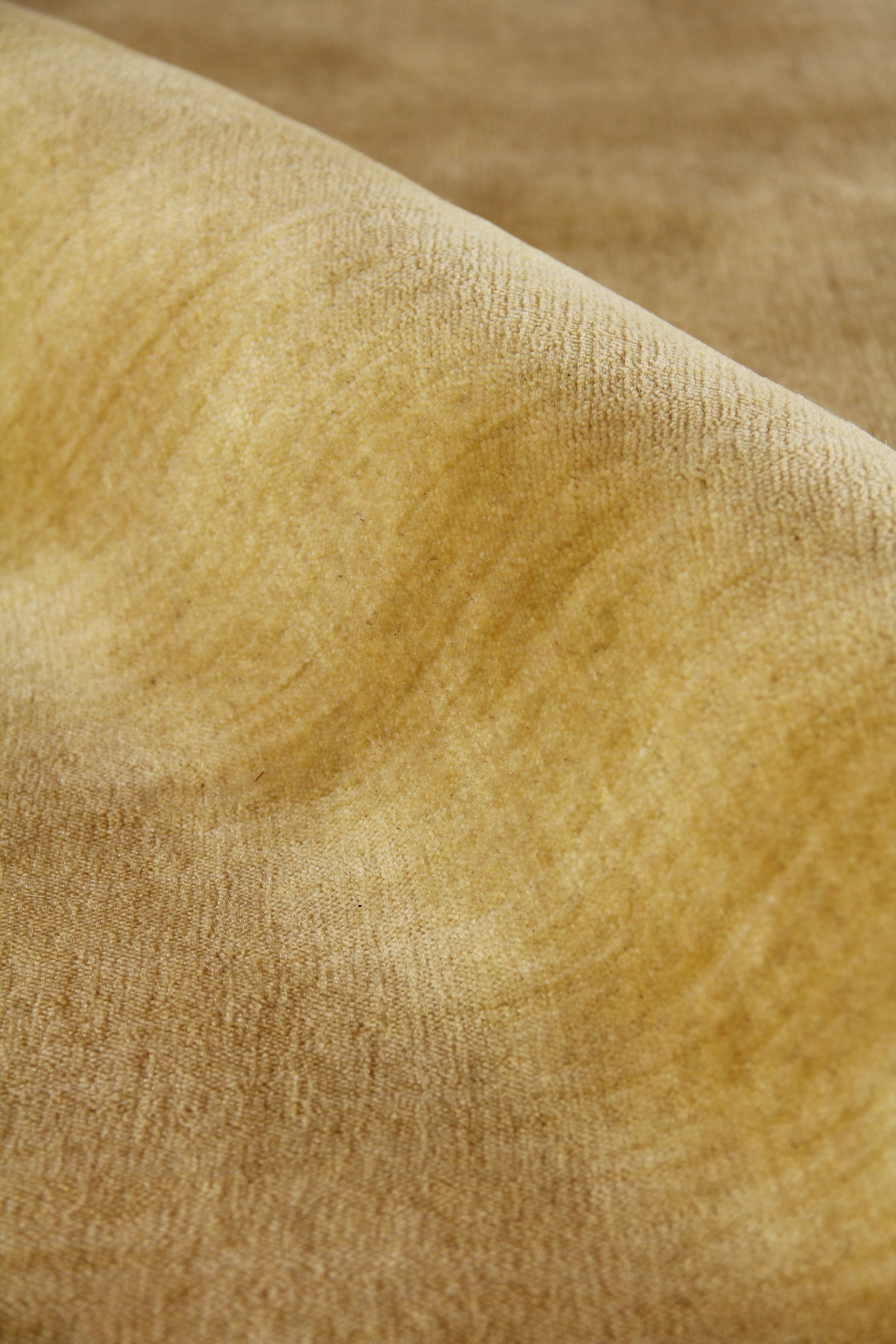 Close-up of warm golden-tan wool rug fibers with a soft nap and curving folds.
