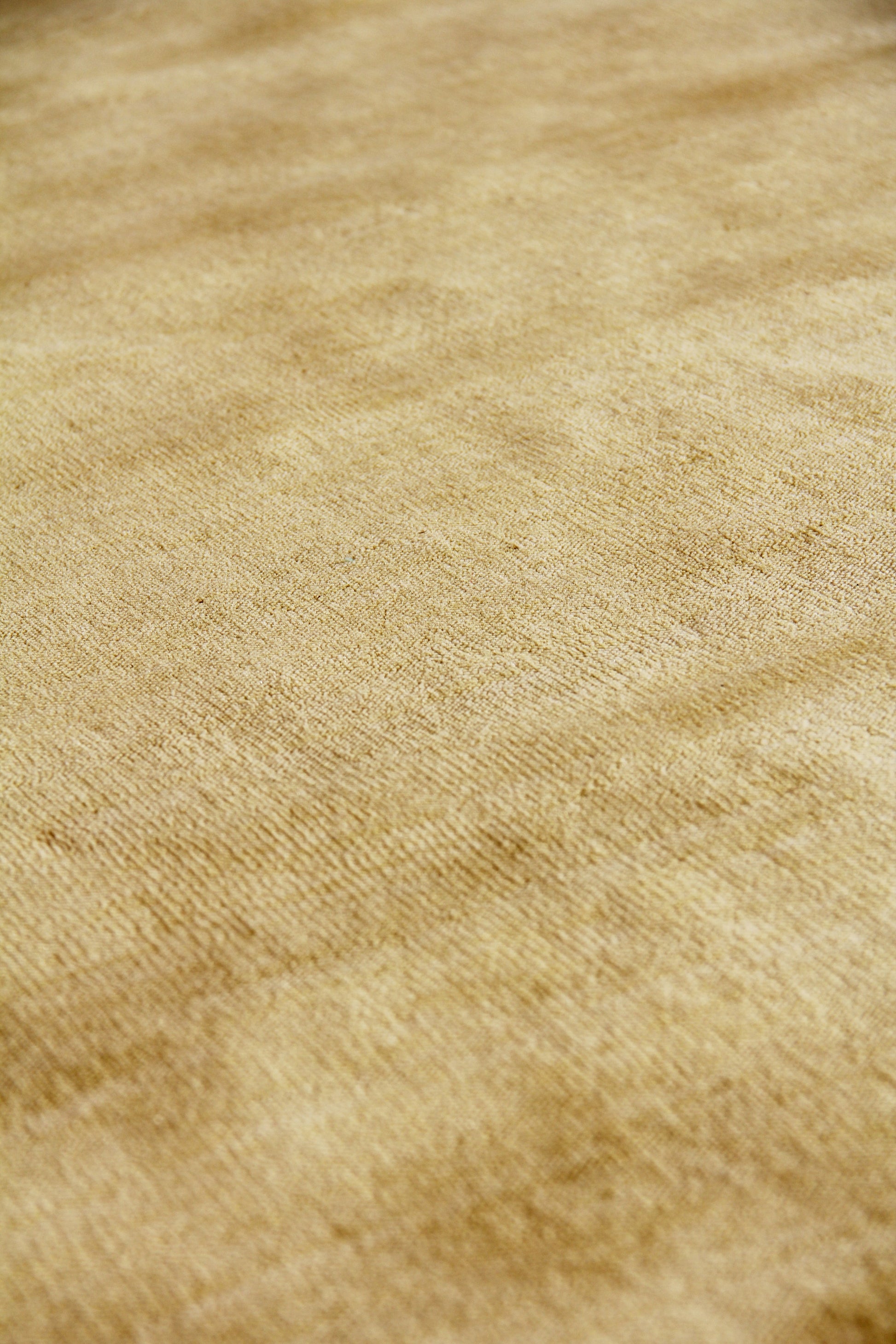 Beige wool rug close-up showing a soft nap and warm golden-brown tones; hand-loomed weave.