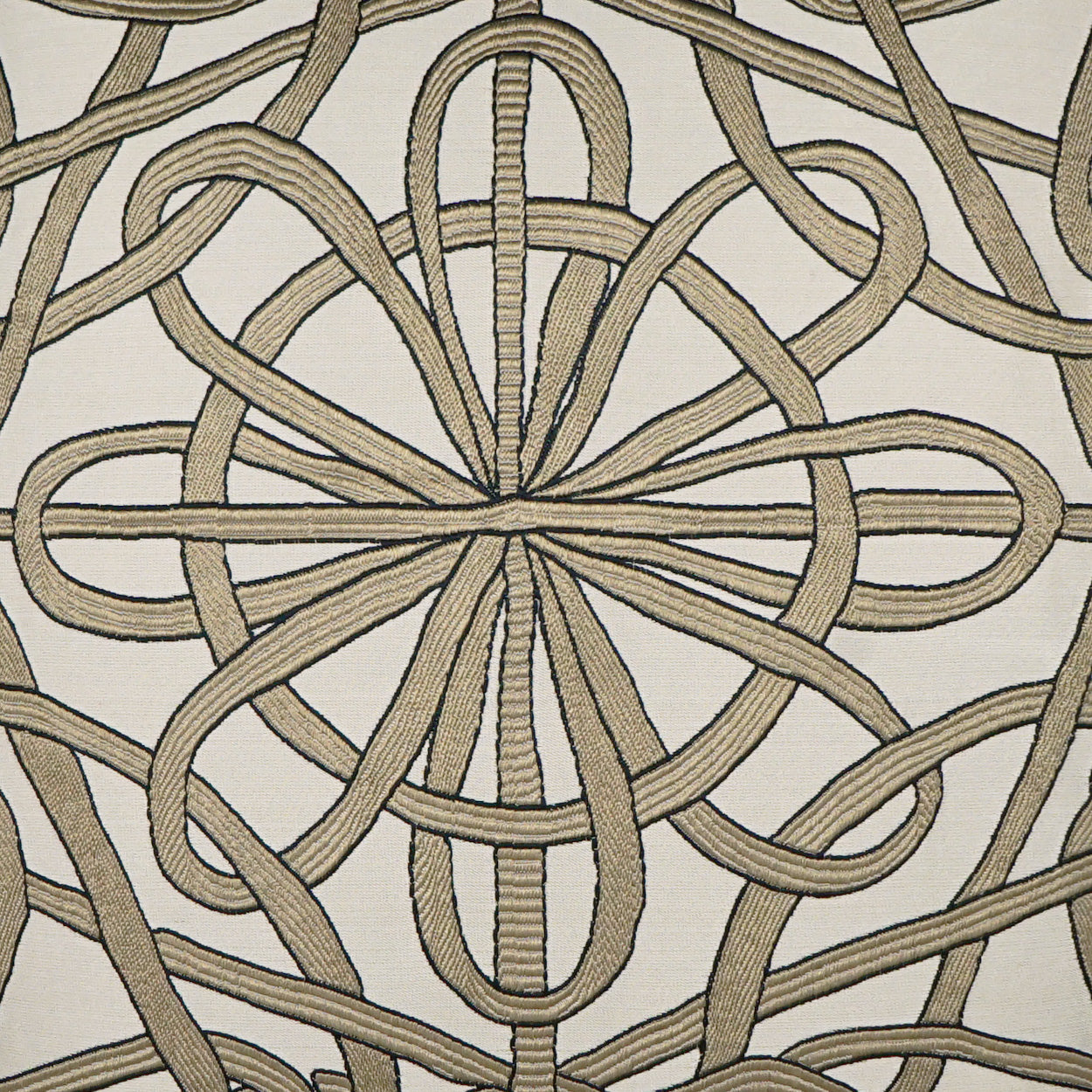 Beige braided rope knot motif forming a circular mandala on off-white fabric; decorative upholstery textile.