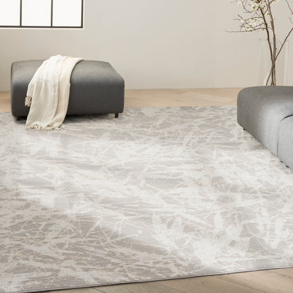 Modern living room with light gray patterned rug, two gray ottomans, a cream throw, and a tall glass vase with branches.