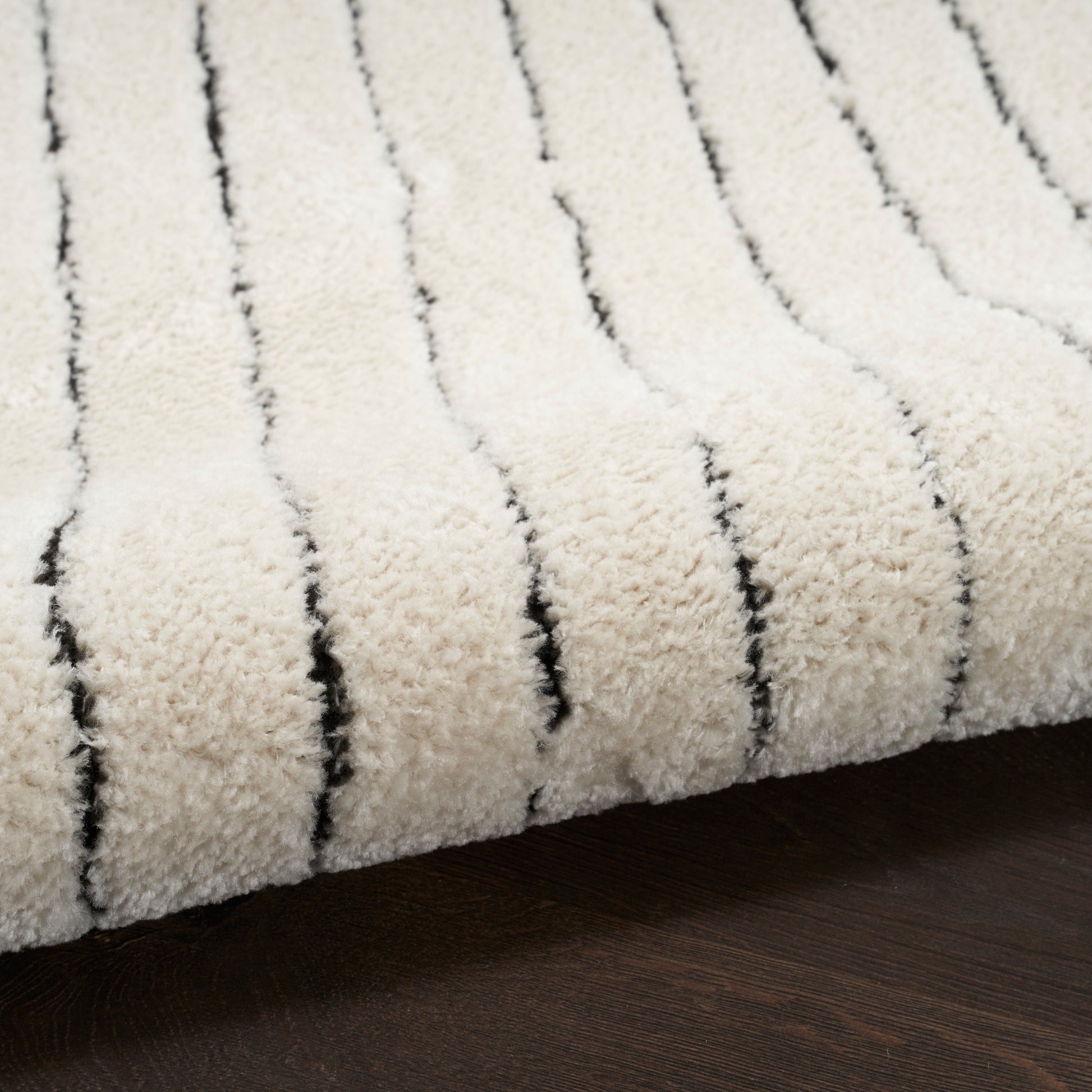 Cream shag rug with narrow black stripes and plush pile, laid on dark wood floor.