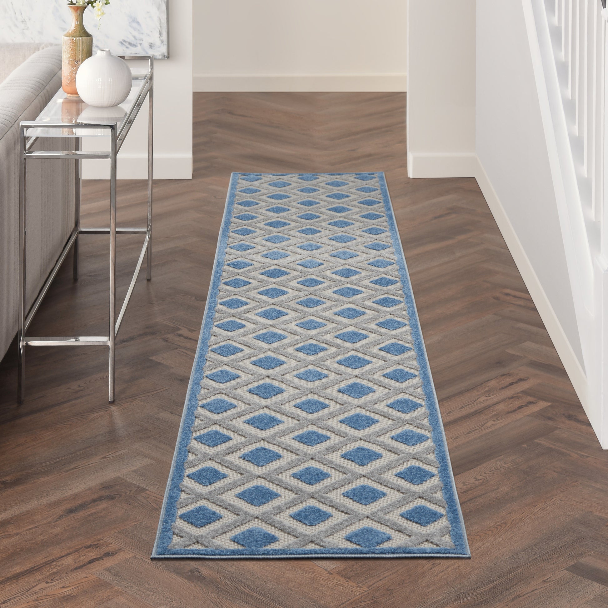 Geometric diamond-pattern hallway runner rug in blue and beige with a light blue border on a dark wood floor.
