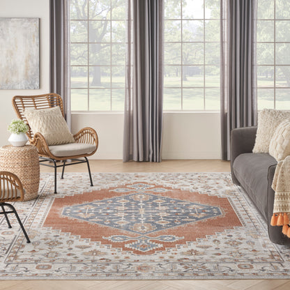 Bright living room with oriental-style rug in blue, rust, and ivory; rattan chair, gray sofa, beige cushions, woven throw.