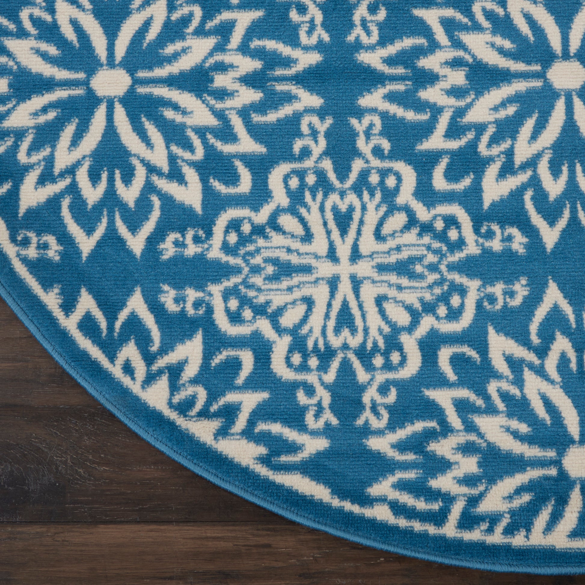 Round teal rug with white mandala floral patterns and blue border on dark wood floor.