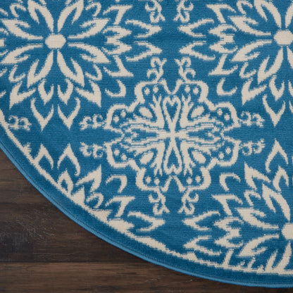 Round teal rug with white mandala floral patterns and blue border on dark wood floor.
