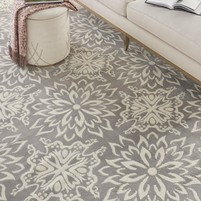 Gray rug with large cream floral medallion pattern in a cozy living room; round cream ottoman with a pink throw.