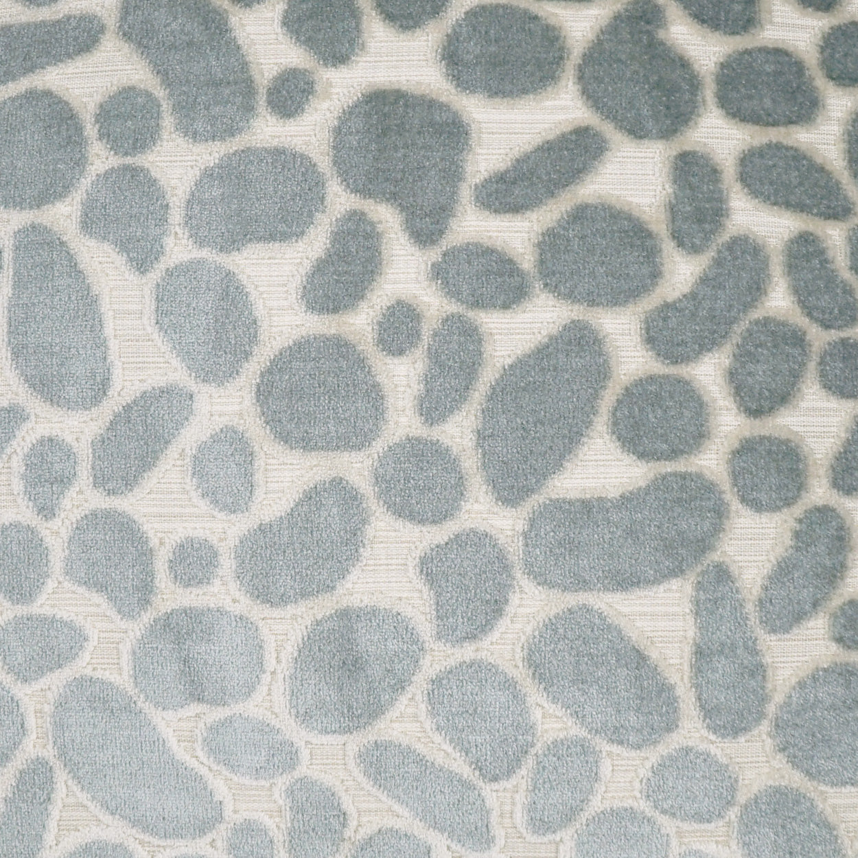 Soft beige pillow cover with blue-gray pebble shapes in a scattered organic pattern and a subtle woven texture.