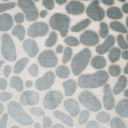 Soft beige pillow cover with blue-gray pebble shapes in a scattered organic pattern and a subtle woven texture.