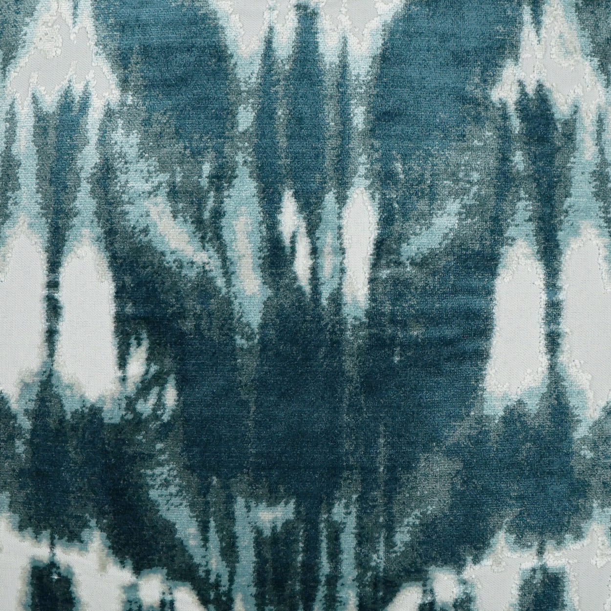 Ikat-inspired teal and white fabric with bold vertical abstract motifs; woven textile for upholstery or drapery.