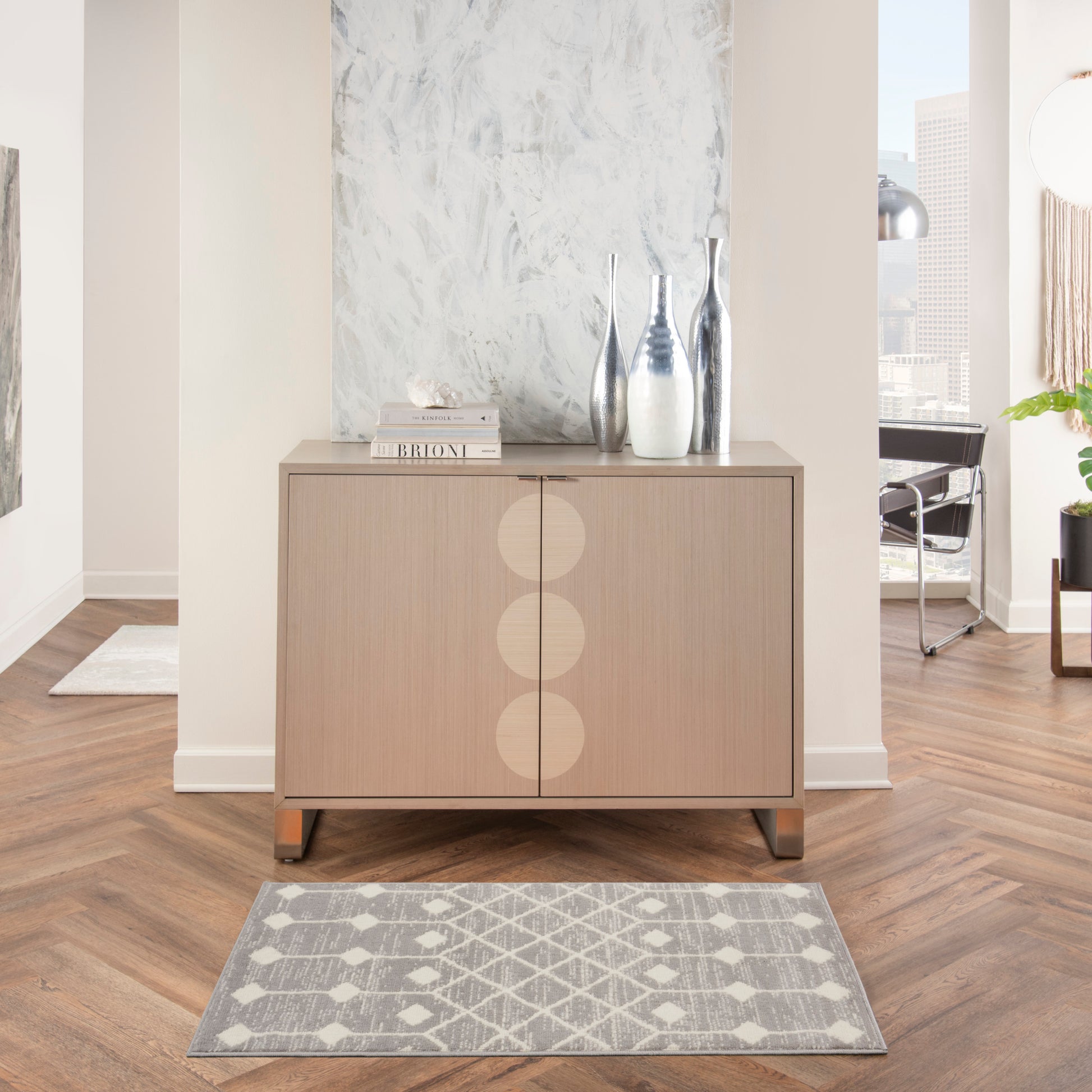 Light wood sideboard with three circular panel details, top decor of vases and books, and a gray geometric rug in front.