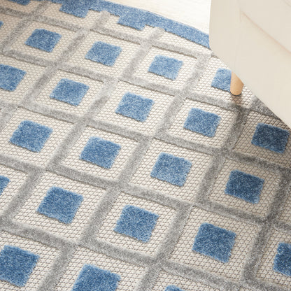 Soft-pile round area rug with blue square motifs in a gray grid, geometric pattern beside a white chair.