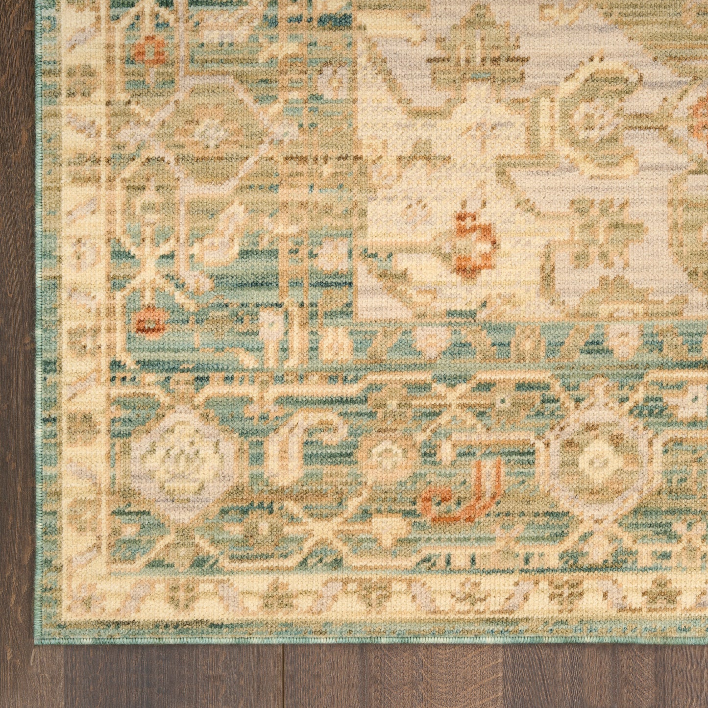 Partial view of a traditional oriental runner rug with teal border, cream field and floral motifs on dark wood floor.