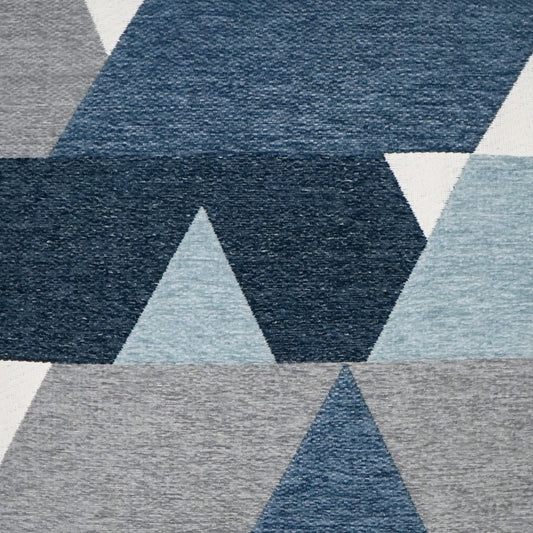 Geometric blue-gray area rug featuring triangles and parallelograms in denim, slate and light gray tones; woven texture.