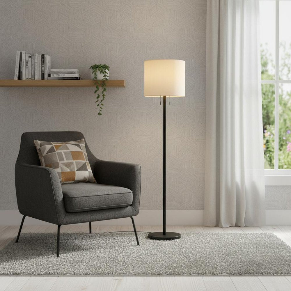 Gray fabric armchair with geometric cushion, light rug, black floor lamp, wall shelf with books & plant, sheer window.
