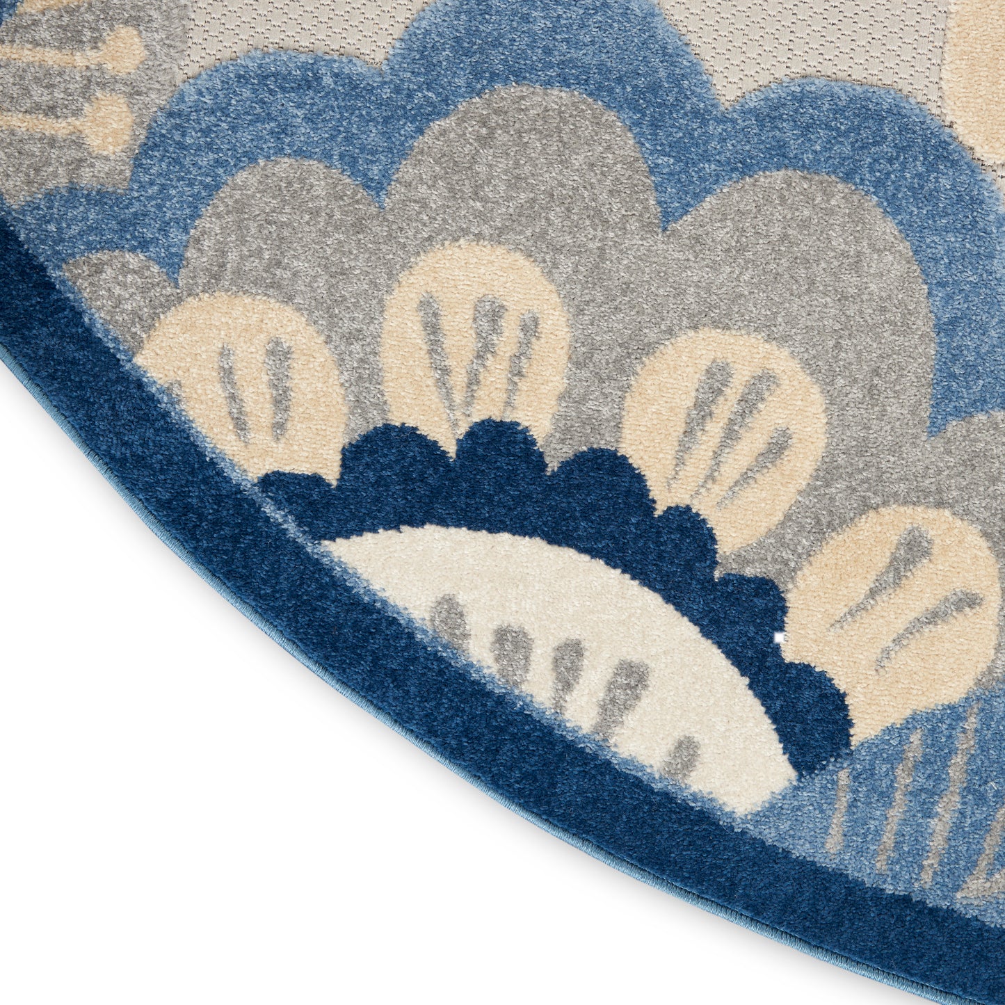 Round rug with blue, cream and beige scallop motif; textured woven surface and curved edge visible.