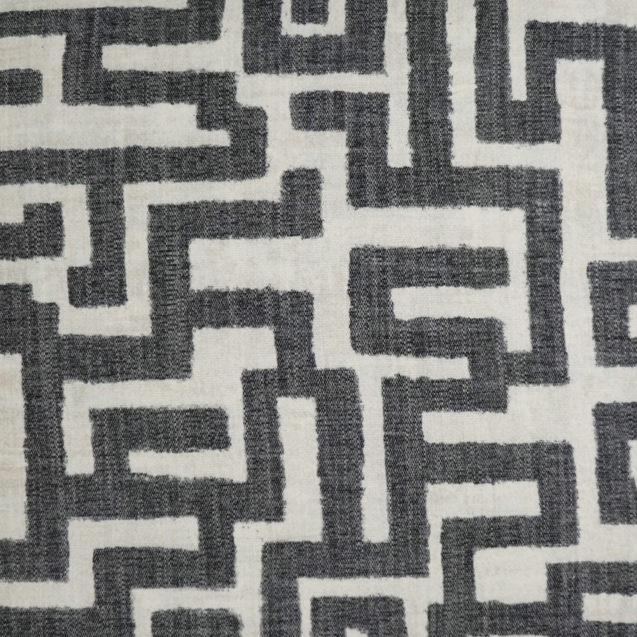 Woven upholstery fabric with a charcoal gray maze-like geometric pattern on a light beige background.