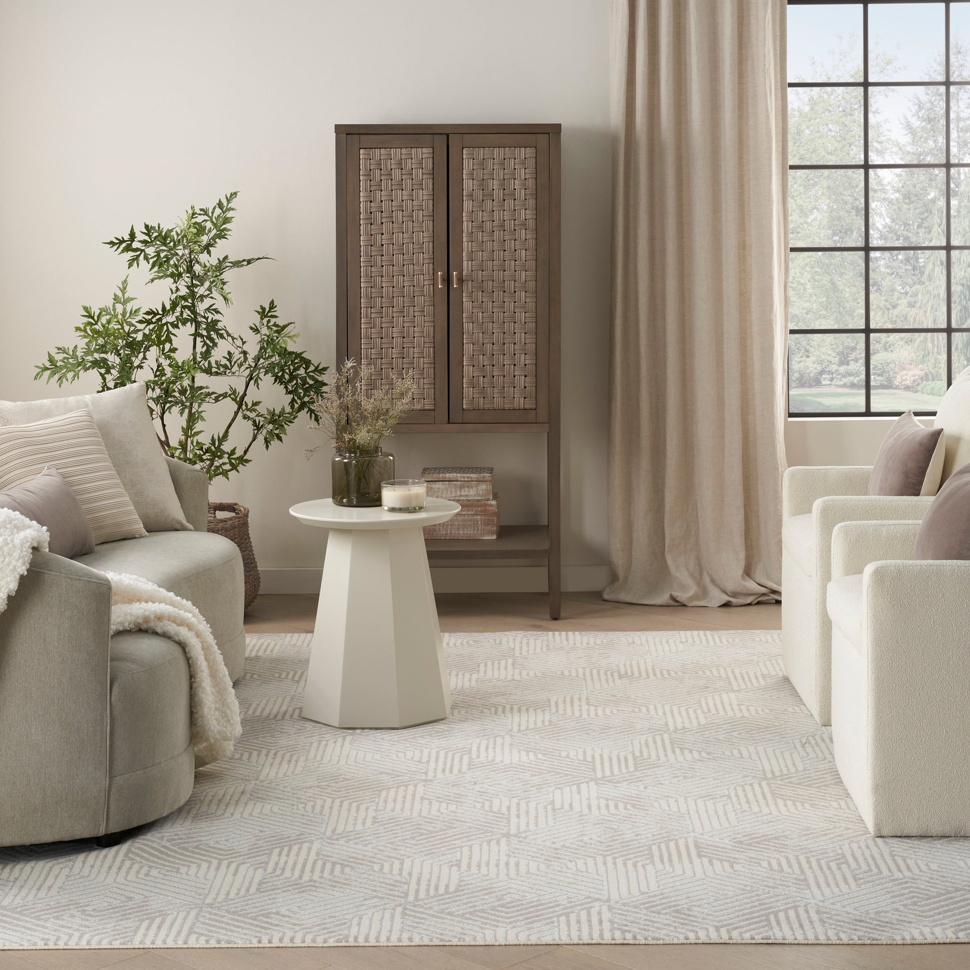 Neutral living room with cream sofas, woven cabinet, white pedestal table, potted greenery, beige curtains, patterned rug.