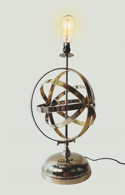 Brass-toned armillary-sphere desk lamp with Edison bulb; circular metal rings on a round metal base, vintage industrial decor.