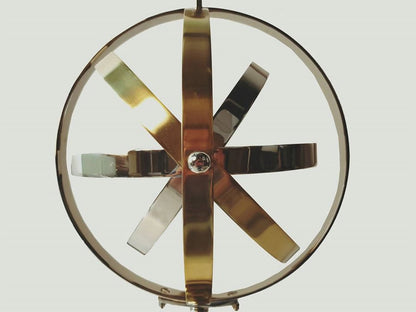 Circular metal wind spinner with six brass, copper and silver blades around a central gem and ring frame.