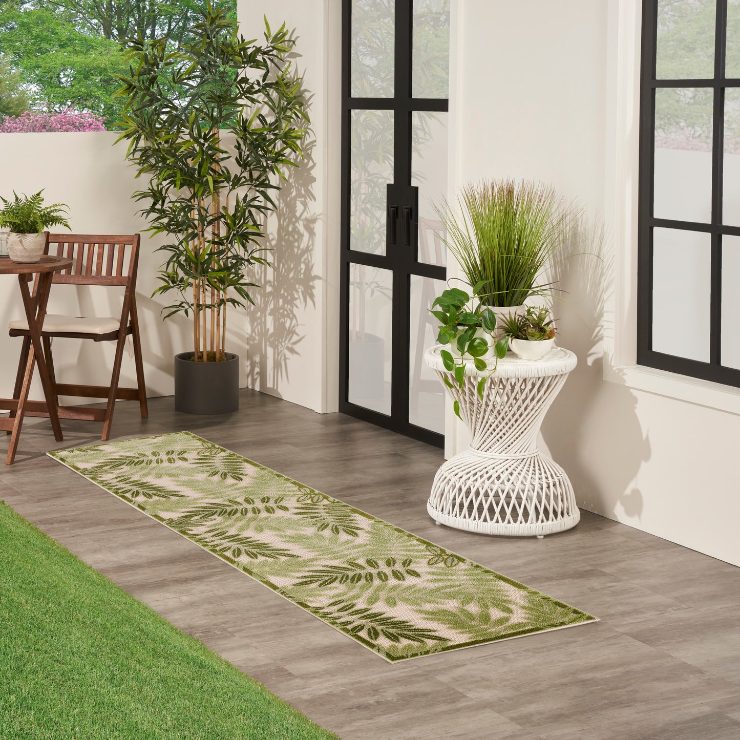 Green botanical leaf-pattern runner rug on wood-look tile beside potted plants and black-framed glass doors