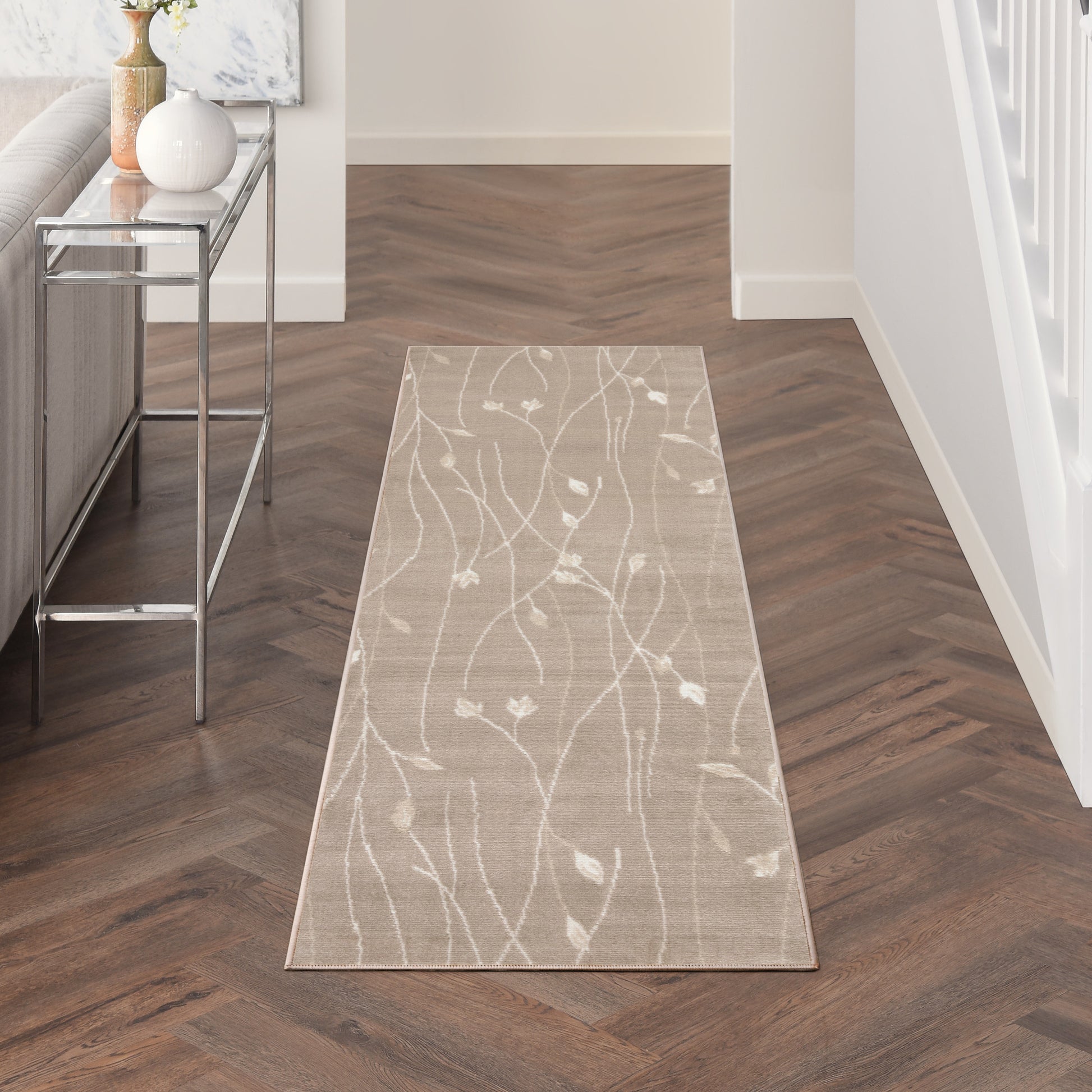 Beige runner rug with white botanical vine pattern on dark herringbone wood floor in entryway.