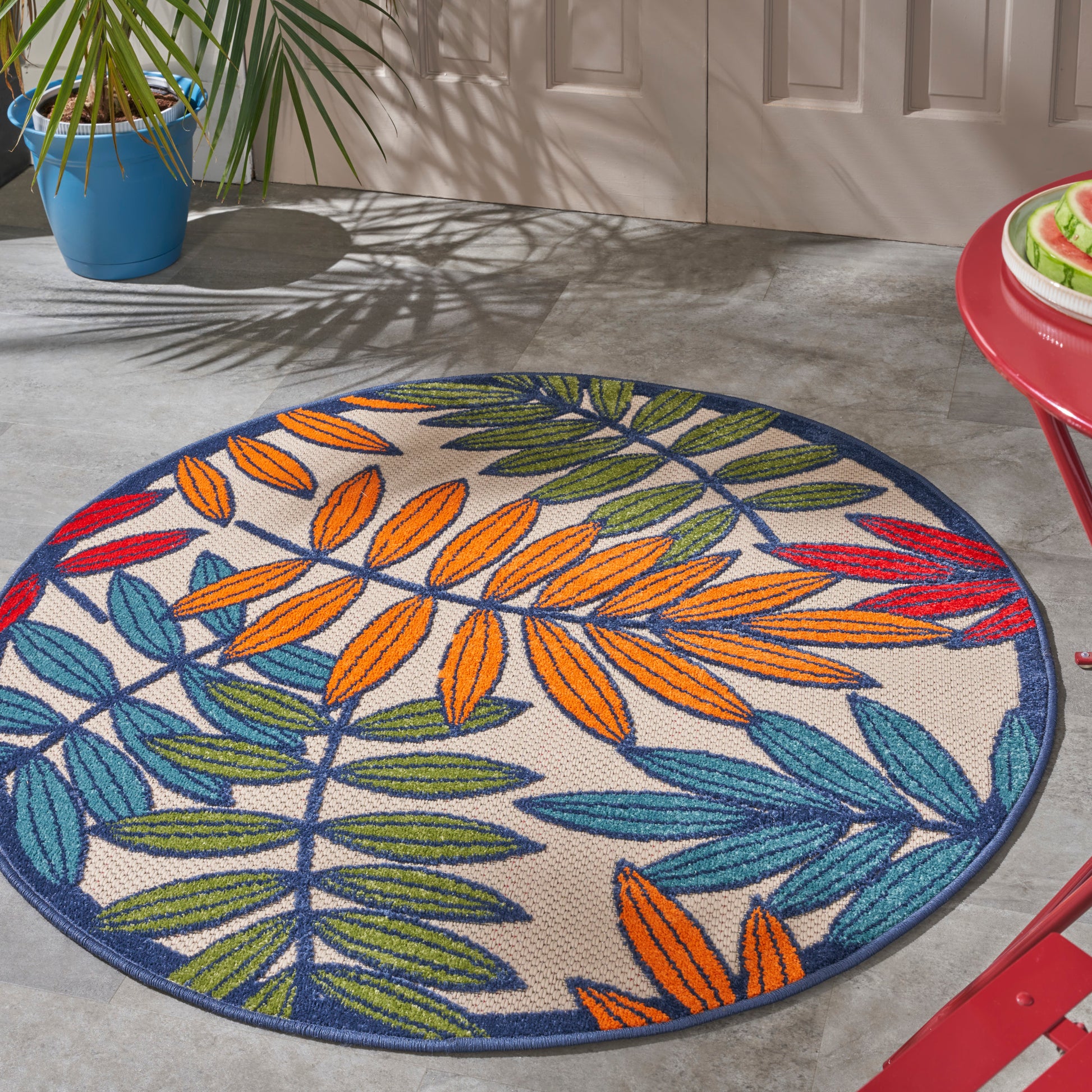 Round outdoor rug with multicolored leaf motif (orange, red, blue, green) on beige, navy border.
