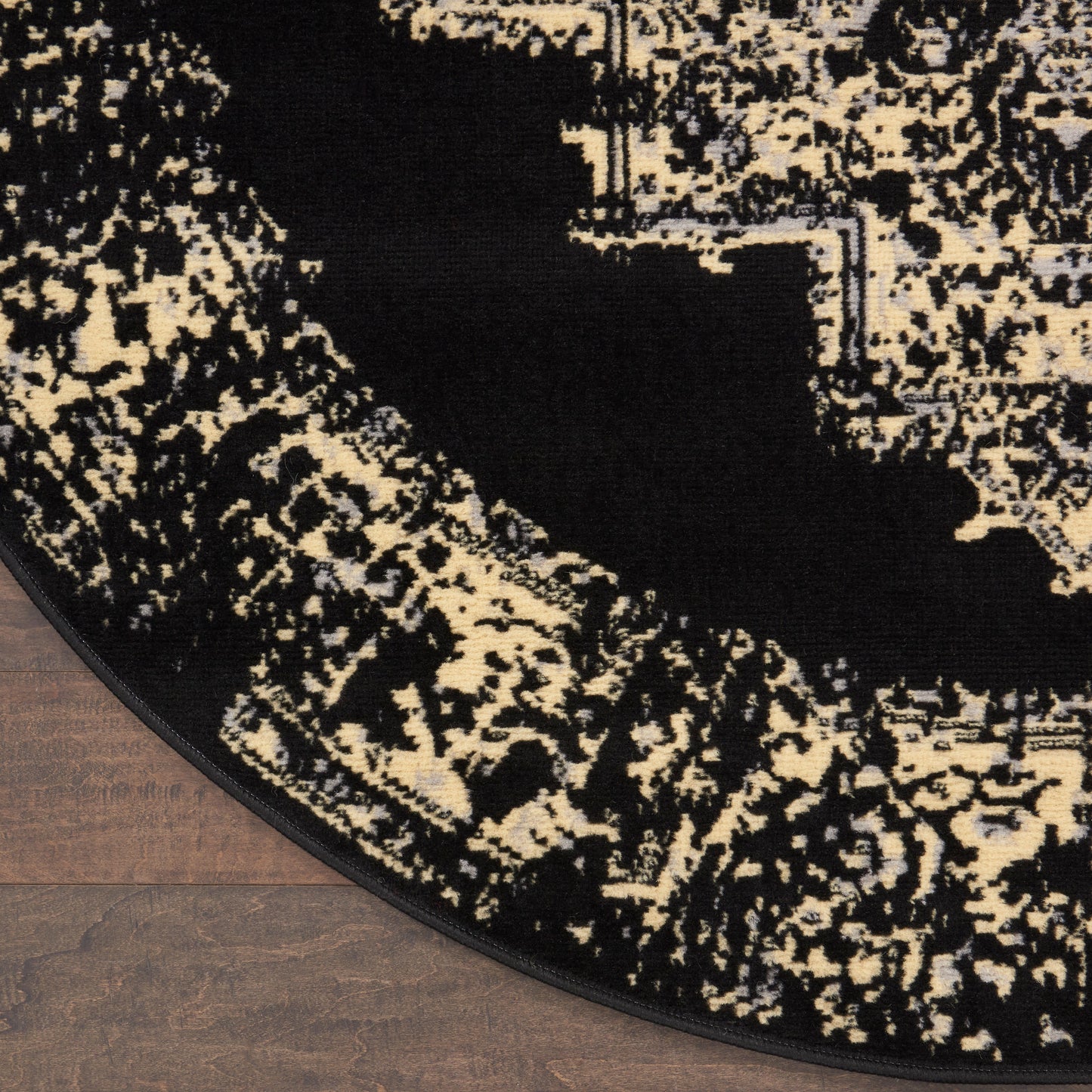 Round black and cream abstract patterned rug with textured weave on wood floor.