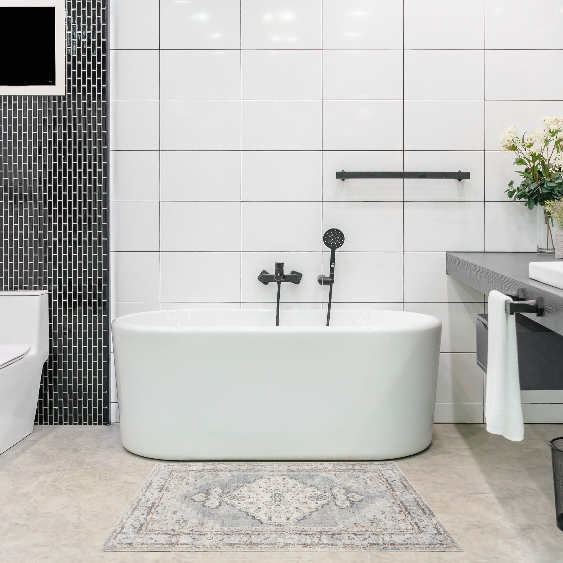 White freestanding oval bathtub with black fixtures in a modern tiled bathroom, featuring a black mosaic wall and vanity.